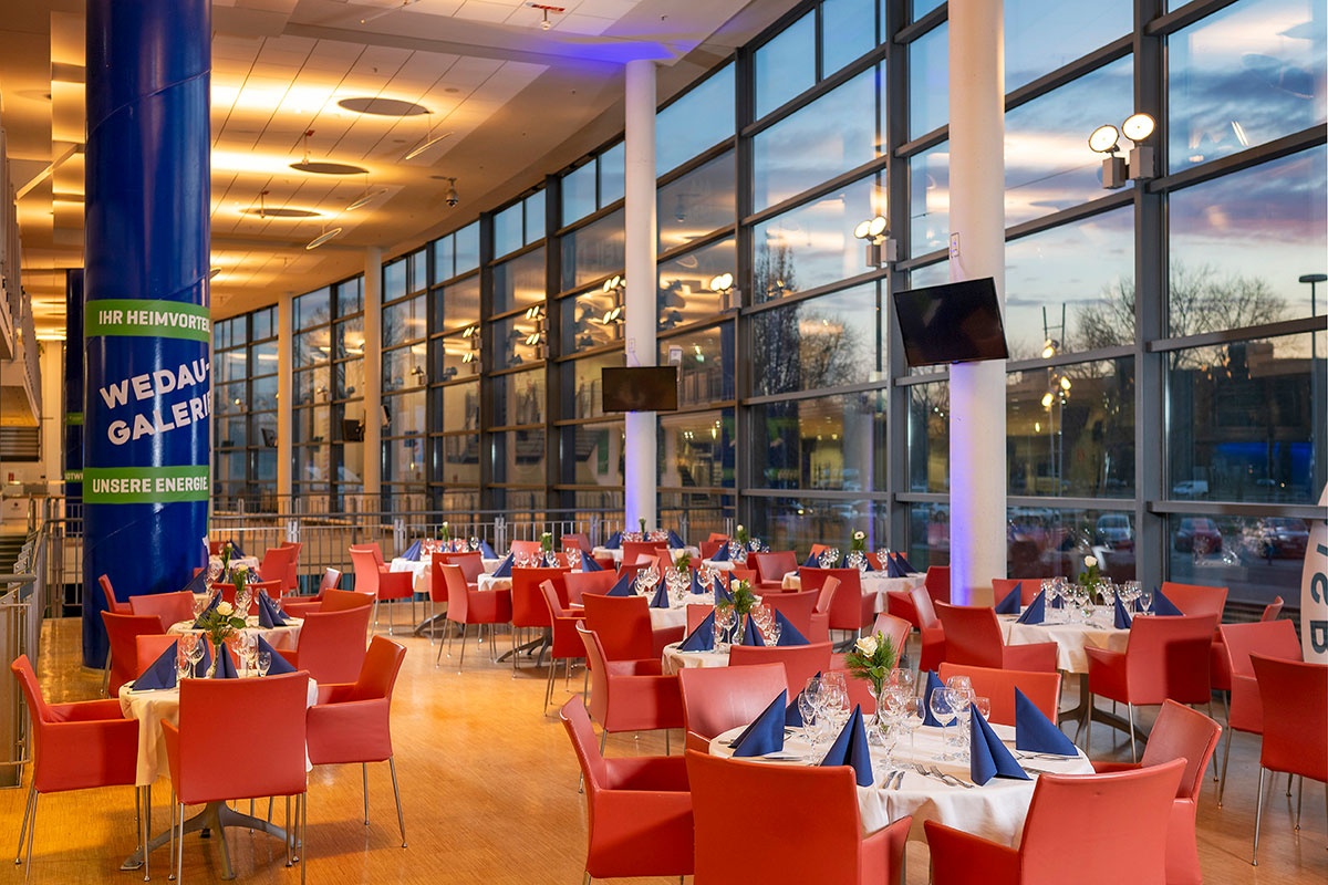 Die Business Lounge mit vielen runden Tischen, roten Stühlen und einer großen Fensterfront rechts.