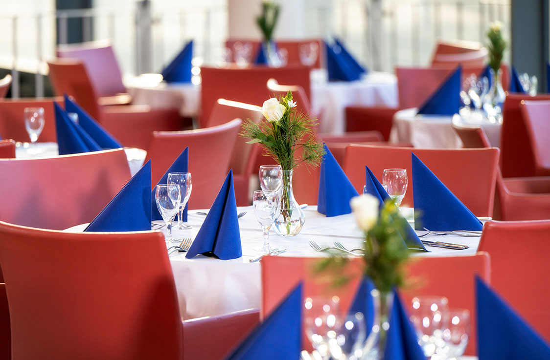 Vielen runde Tische, eingedeckt mit roten Stühlen und blauen Servietten.