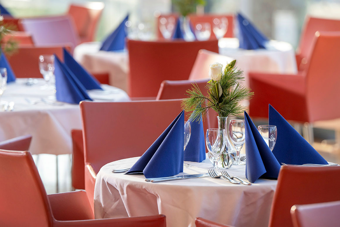 Vielen runde Tische, eingedeckt mit roten Stühlen und blauen Servietten.