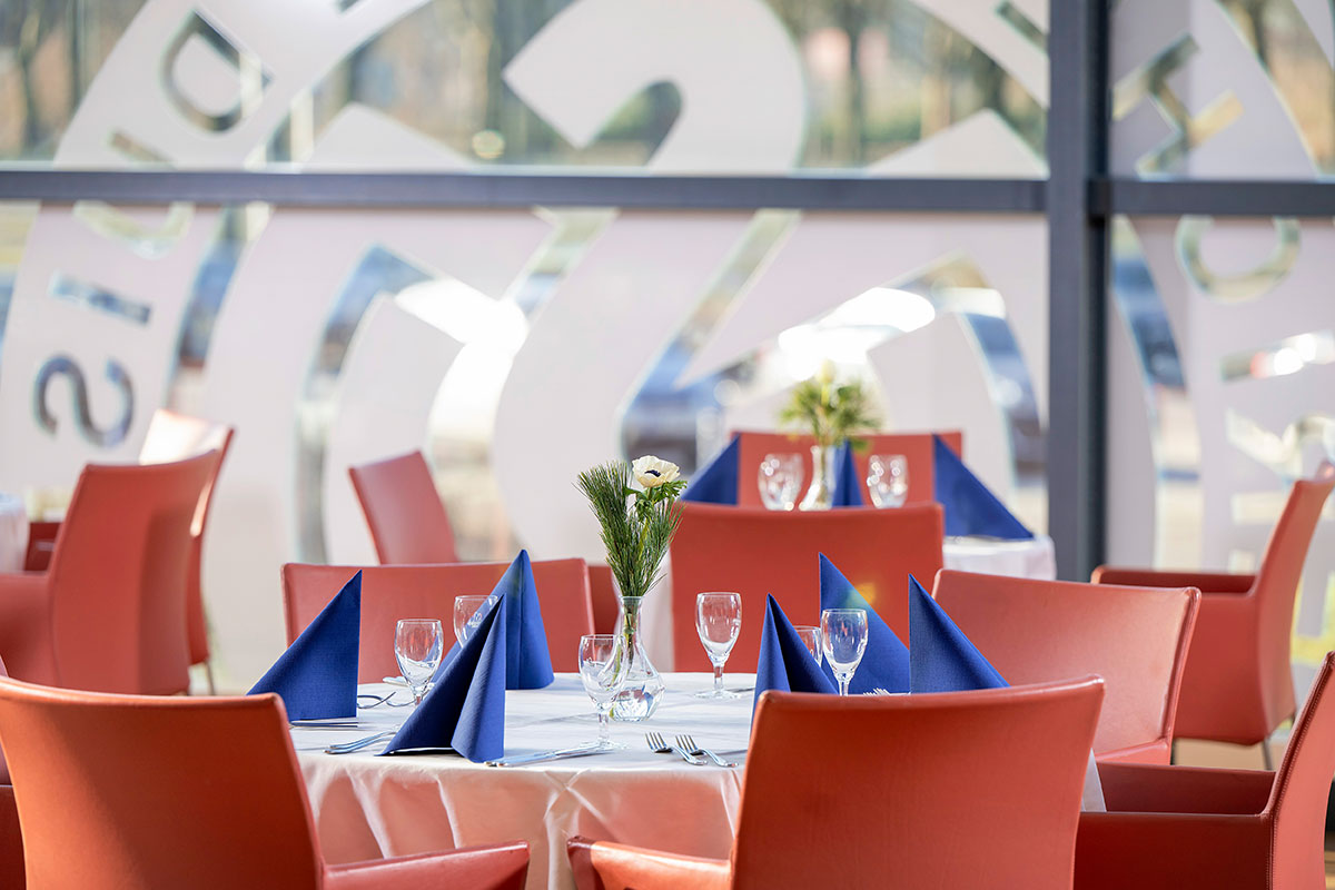 Eingedeckte Tische mit roten Stühlen, im Hintergrund das "MSV Duisburg"-Logo auf einer großen Fensterscheibe.