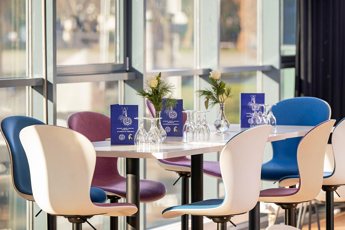 Eine Lounge mit weißen Tischen und Stühlen sowie blauen Menükarten des MSV-Duisburg auf den Tischen.