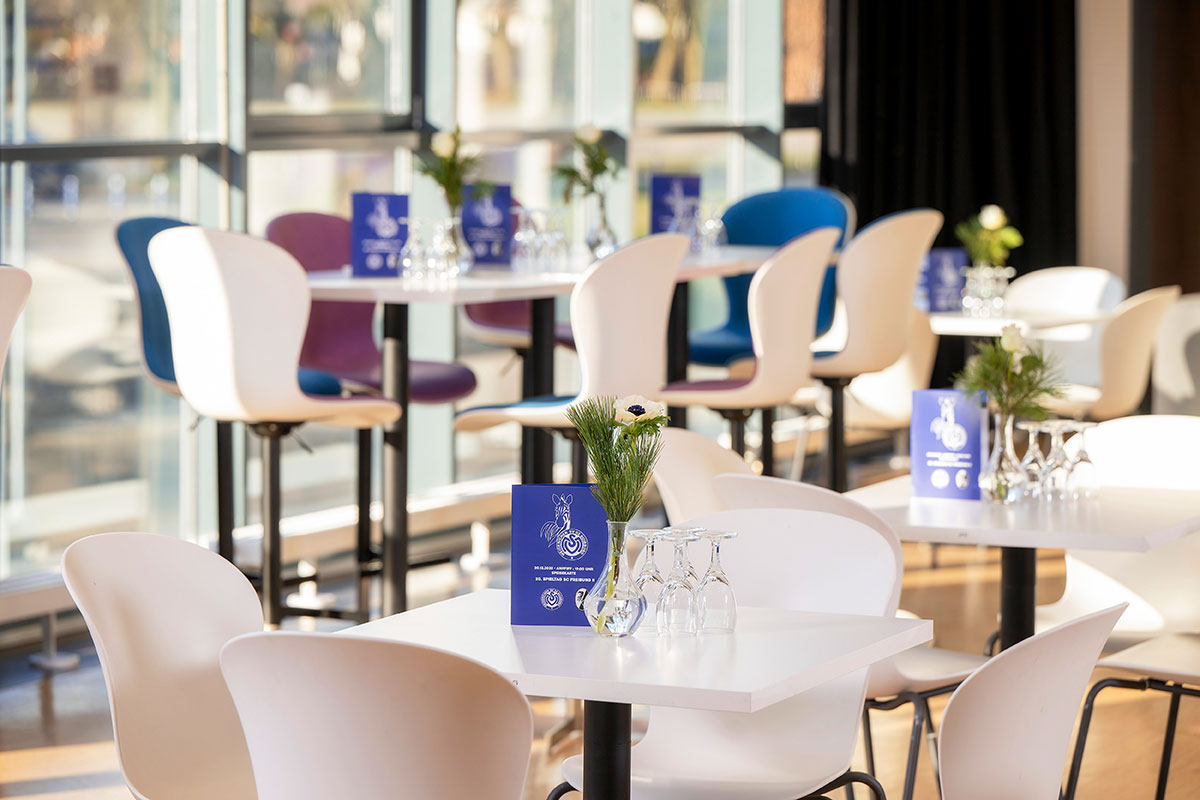 Eine Lounge mit weißen Tischen und Stühlen sowie blauen Menükarten des MSV-Duisburg auf den Tischen.