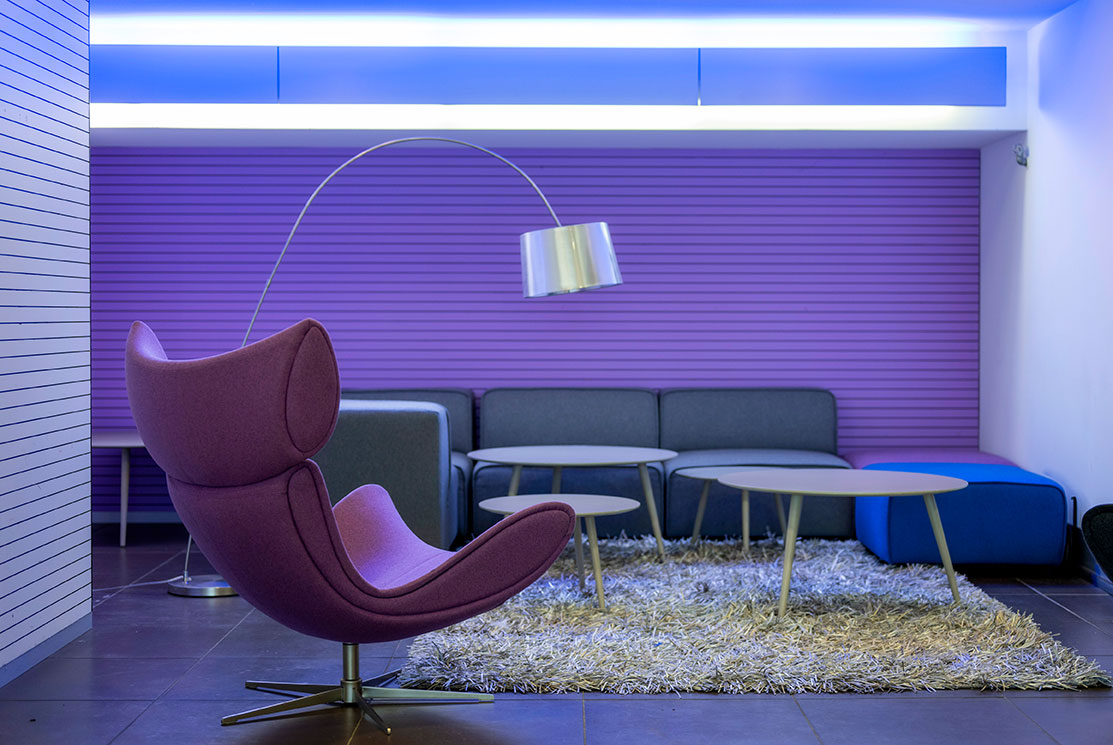  Ein lila Lounge-Bereich mit einem Sessel, einem Sofa, Couchtischen und einer Stehlampe.