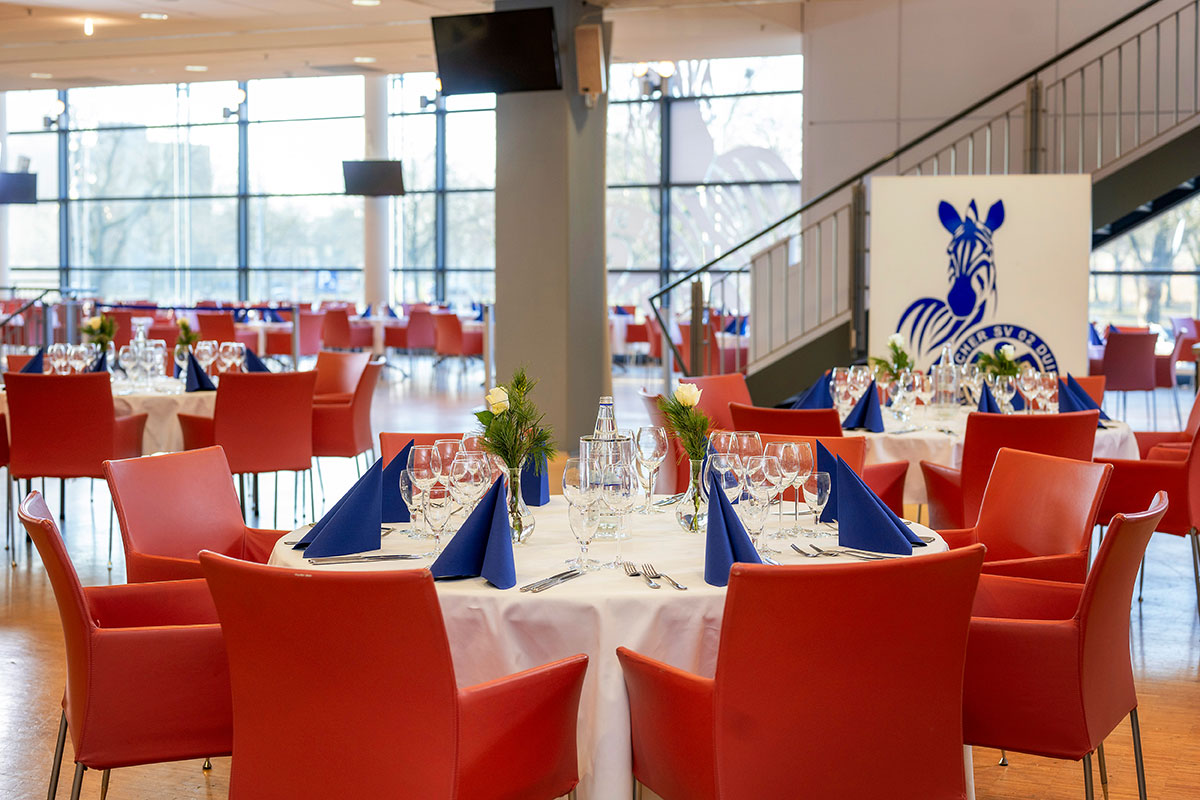 Festlich gedeckte Tische mit Gläsern, blauen Servietten und einem Banner mit Zebra-Logo im Hintergrund.