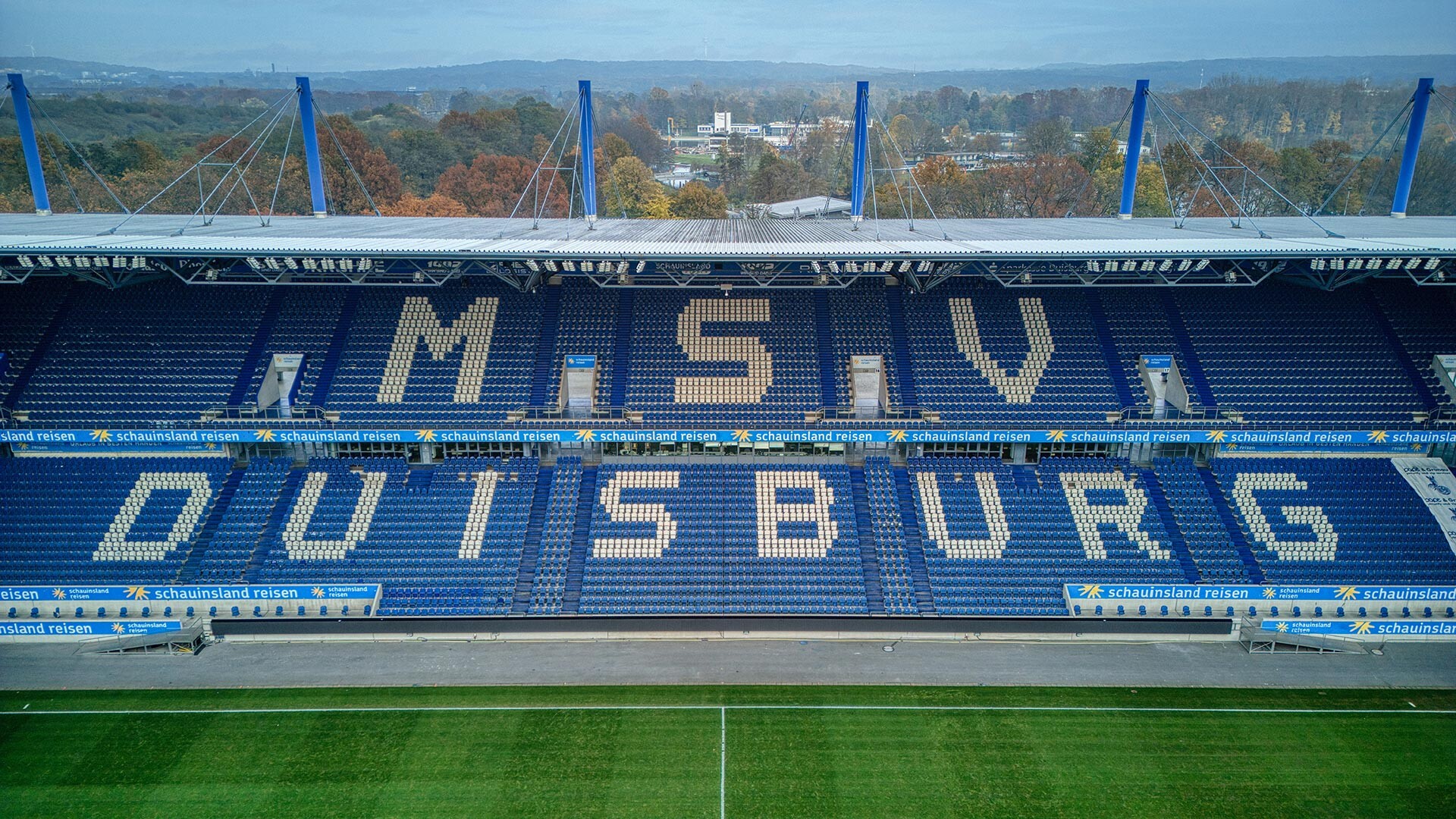 Blick auf Stadionränge mit blauen Sitzen, dazwischen weiße Sitze, die "MSV DUISBURG" bilden und ein grünes Spielfeld davor.