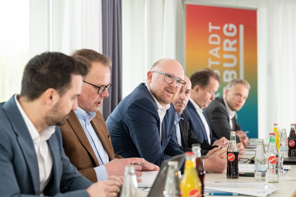 Sechs Männer im Anzug sitzen an einem Konferenztisch. Auf dem Tisch stehen Getränke von Sinalco.